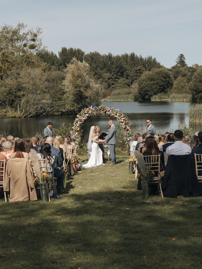 An outdoor lakeside wedding ceremony - guests seated on the lawn before a floral arch